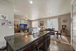 Kitchen with dark wood-style floors, ceiling fan, hanging light fixtures, open floor plan, and dark stone counters