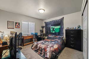 Carpeted bedroom featuring a desk and a textured ceiling