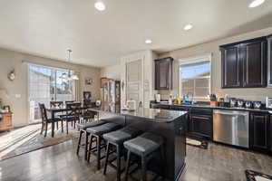 Kitchen featuring stainless steel dishwasher, a sink, a breakfast bar area, a chandelier, and dark wood-style flooring