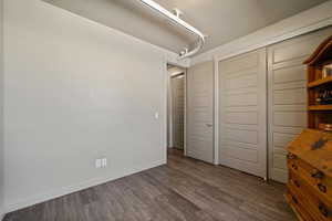 Unfurnished bedroom featuring dark wood finished floors, baseboards, and a closet
