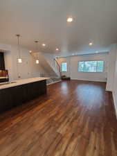 Unfurnished living room with a sink, stairway, dark wood-style flooring, recessed lighting, and baseboards