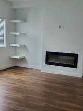 Unfurnished living room featuring a glass covered fireplace, wood finished floors, and baseboards