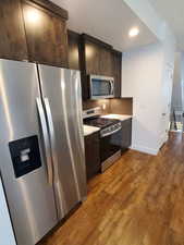 Kitchen with stainless steel appliances, light countertops, dark brown cabinets, wood finished floors, and recessed lighting
