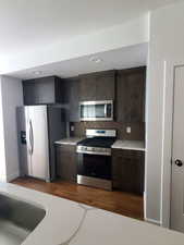 Kitchen with appliances with stainless steel finishes, light countertops, tasteful backsplash, dark brown cabinetry, and dark wood finished floors