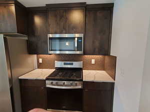 Kitchen with appliances with stainless steel finishes, tasteful backsplash, dark brown cabinets, and modern cabinets