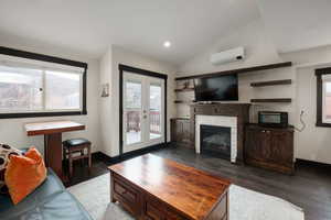 Living room with wood-type flooring, vaulted ceiling, an AC wall unit, recessed lighting, and a stone fireplace