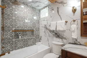 Bathroom with tile walls, toilet, vanity, and shower / bathtub combination