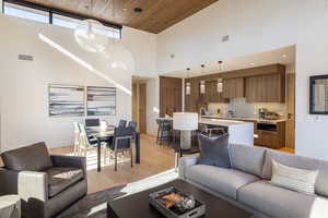 Living room featuring wooden ceiling, a high ceiling, light wood-type flooring, and a chandelier