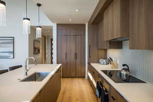Kitchen with brown cabinetry, pendant lighting, light wood-style floors, light stone counters, and black electric cooktop