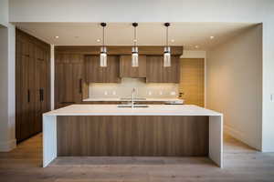 Kitchen with modern cabinets, a sink, a large island, tasteful backsplash, and baseboards