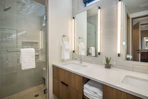 Bathroom featuring a stall shower, double vanity, and tasteful backsplash