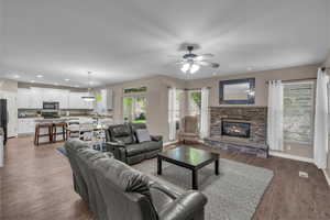 Living room with a ceiling fan, a stone fireplace, light wood finished floors, and recessed lighting