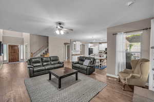 Living area with ceiling fan, stairway, light wood-style floors, and arched walkways