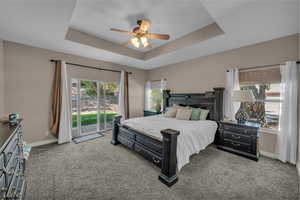 Bedroom featuring a raised ceiling, carpet flooring, access to exterior, and ceiling fan