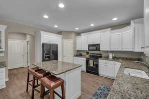 Kitchen with black appliances, a breakfast bar area, white cabinets, light stone countertops, and recessed lighting