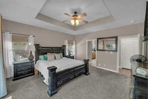 Carpeted bedroom with a tray ceiling, a ceiling fan, and ensuite bath