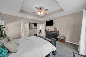 Carpeted bedroom featuring a tray ceiling and a ceiling fan