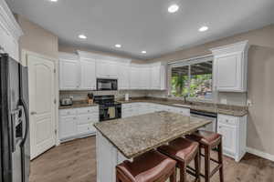Kitchen featuring black appliances, a breakfast bar, light wood finished floors, white cabinets, and recessed lighting