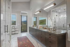 Bathroom featuring double vanity, plenty of natural light, a marble finish shower, marble finish flooring, and a high ceiling
