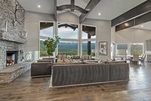 Living area featuring high vaulted ceiling, a stone fireplace, dark wood-type flooring, beamed ceiling, and a ceiling fan