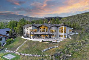 Back of property at dusk with a patio area, a chimney, a deck with mountain view, and dirt driveway