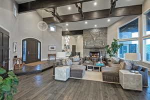 Living area with high vaulted ceiling, beam ceiling, dark wood-type flooring, arched walkways, and a stone fireplace