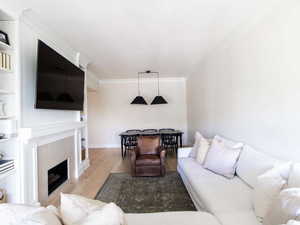 Living room featuring wood finished floors, crown molding, a tiled fireplace, and baseboards