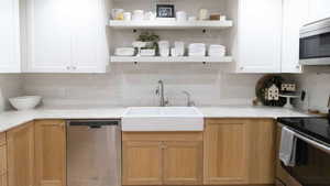 Kitchen featuring stainless steel appliances, open shelves, a sink, tasteful backsplash, and light countertops