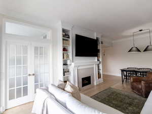 Living room featuring ornamental molding, wood finished floors, baseboards, a tile fireplace, and built in shelves
