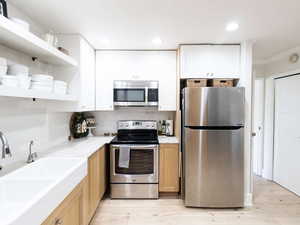 Kitchen with stainless steel appliances, a sink, open shelves, backsplash, and white cabinets