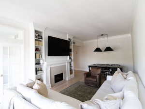 Living room featuring wood finished floors, crown molding, a tiled fireplace, built in shelves, and baseboards