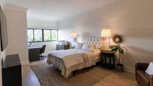 Bedroom featuring light wood finished floors, crown molding, baseboards, and a desk