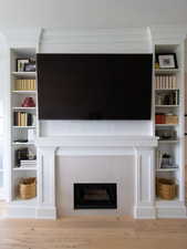 Detailed view of a tiled fireplace, wood finished floors, and ornamental molding
