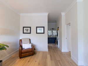 Sitting room featuring wood finished floors, stacked washing machine and dryer, crown molding, and baseboards