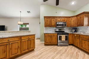 Kitchen featuring appliances with stainless steel finishes, brown cabinetry, light wood-type flooring, backsplash, and lofted ceiling