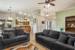 Living area with ceiling fan, vaulted ceiling, and light wood-style floors