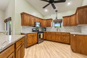 Kitchen with stainless steel appliances, a sink, brown cabinets, light wood finished floors, and light stone countertops
