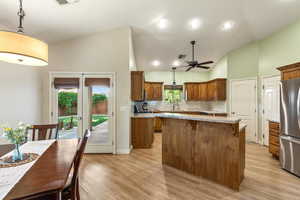 Kitchen featuring freestanding refrigerator, lofted ceiling, brown cabinets, tasteful backsplash, and ceiling fan
