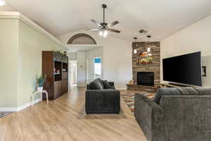 Living area featuring a ceiling fan, light wood-style floors, a stone fireplace, baseboards, and high vaulted ceiling