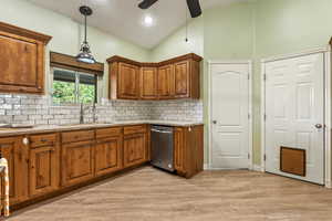 Kitchen featuring dishwasher, a sink, vaulted ceiling, brown cabinets, and backsplash
