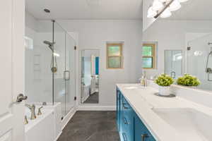 Bathroom featuring a shower stall, double vanity, a garden tub, and baseboards