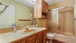 Bathroom featuring wallpapered walls, vanity, toilet, and combined bath / shower with glass door