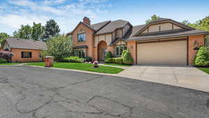 English style home featuring concrete driveway, brick siding, a chimney, and an attached garage