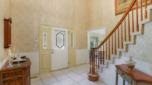 Entrance foyer with stairs, light tile patterned floors, a wainscoted wall, and a towering ceiling