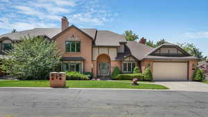 Tudor home with a chimney, an attached garage, a front yard, and concrete driveway