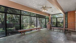 Unfurnished sunroom featuring stone tile flooring, a ceiling fan, and a textured ceiling