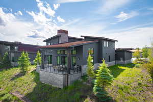 Rear view of property with stone siding, a chimney, a patio area, and metal roof