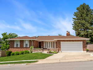Ranch-style house with an attached garage, driveway, a chimney, and brick siding
