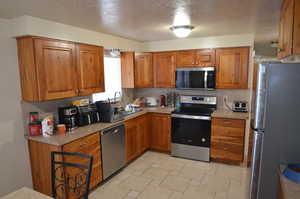 Kitchen featuring stainless steel appliances, brown cabinets, and a textured ceiling