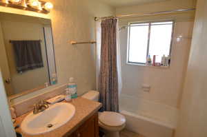 Full bath featuring a textured wall, vanity, toilet, and shower / bath combo